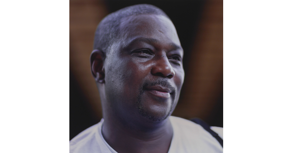 A color photograph of the head and shoulders of a smiling Black man with a goatee and short hair.