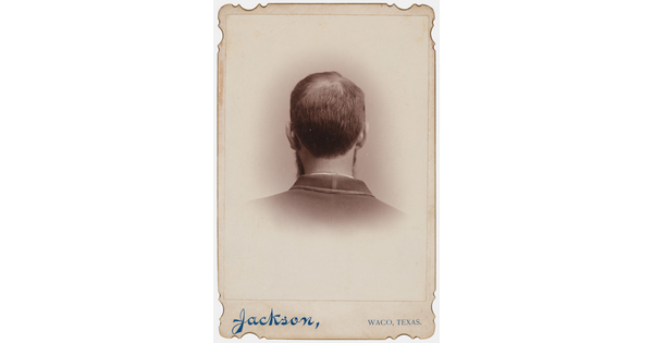 A black-and-white studio portrait photograph of the back of the head, from the neck up, of a man with short hair.