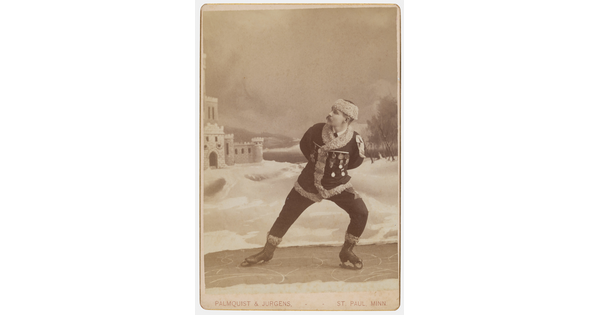 A sepia-toned studio portrait photograph of a White man dressed in winter clothes pretending to ice skate.