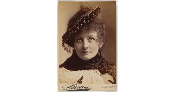 A sepia-toned portrait photograph of a young White woman with curly hair, eyes looking up toward her beaded hat.