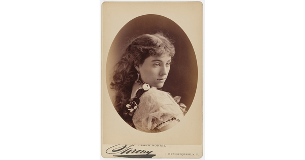 A sepia-toned studio portrait photograph, framed in an oval, of a young White woman gazing over her shoulder.