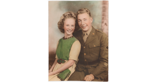 A color photograph of a White woman with curly blonde hair wearing a green and white dress sitting next to a White man in a green military uniform.