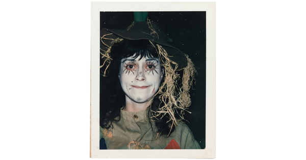 A color portrait of a girl wearing white face paint and dressed as a scarecrow.