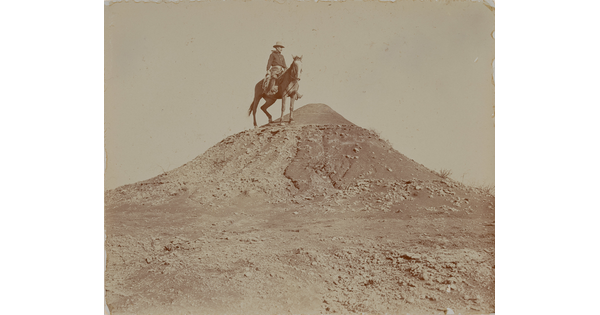 A black-and-white photograph of a man on horseback at the top of a hill.