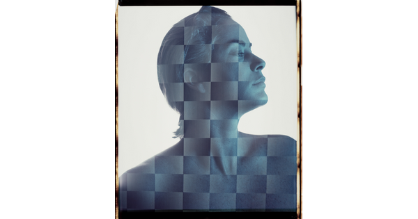 A blue-toned portrait photograph of a White woman with short hair, head turned in profile, as viewed through a checker-board like filter.