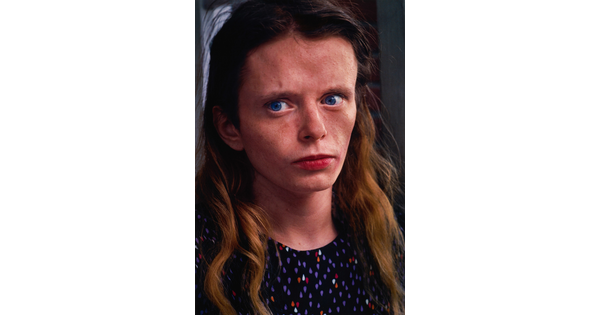 A color portrait photograph of a young White woman with blue eyes looking off to the side, freckles scattered across her face, and long hair wearing a polka-dot top.
