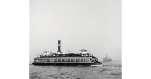 A black-and-white photograph of a large ferryboat on the water under a clear sky.