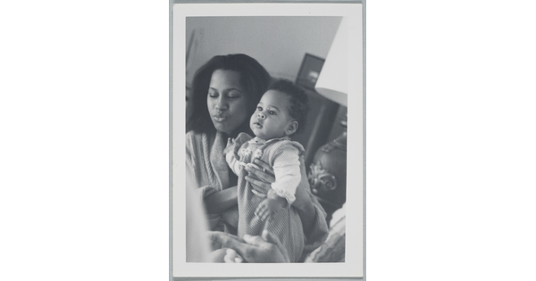 A candid black-and-white photograph of a Black woman holding a baby.
