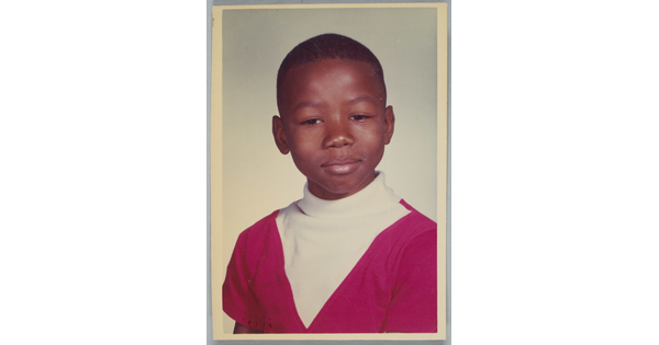 A color school photograph of a Black child with short hair wearing a white and red turtleneck.