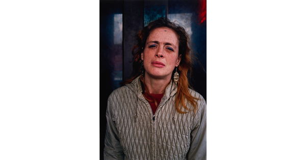 A color portrait photograph of a White woman with long hair squinting and wearing a gray quilted jacket.
