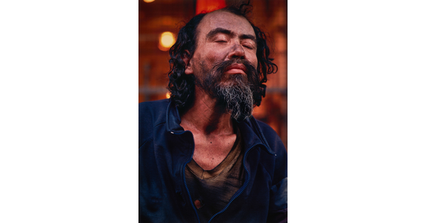 A color portrait photograph of a medium-skinned man with black hair and goatee, eyes closed, dirt smudged on his face, wearing a dark blue jacket.