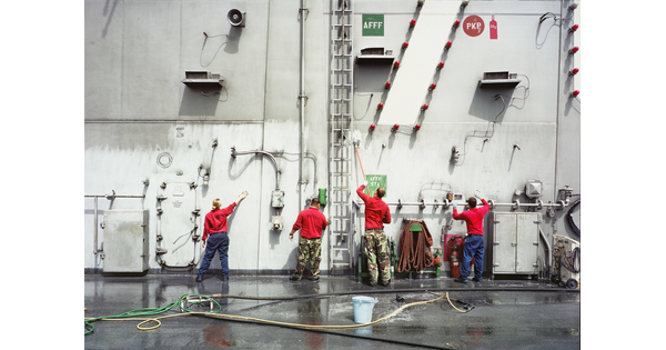 A color photograph of four soldiers washing the side of a large ship.
