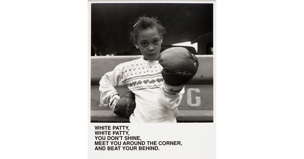A black-and-white photograph of a Black girl wearing boxing gloves, one hand on her hip the other aimed at the viewer, above text that reads, &quot;White Patty, White Patty, You don&#039;t shine. Meet you around the corner and beat your behind.&quot;