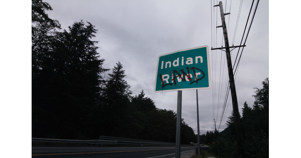 A color photo of a green road sign that says &quot;Indian River&quot; with the word &quot;LAND&quot; spray painted in red over &quot;River.&quot;