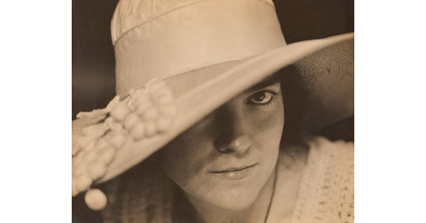 A black-and-white close-up photograph of a White woman wearing a large brimmed hat that covers one of her eyes.