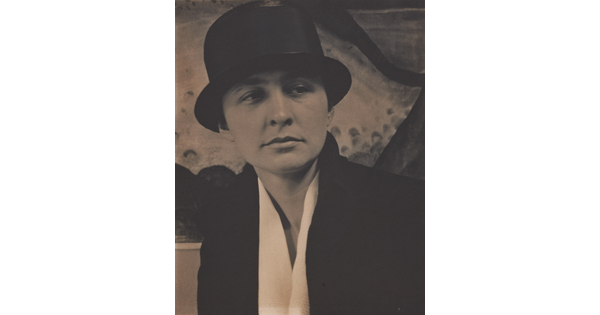 A sepia-toned photograph of a White woman wearing what looks like a top hat, and white blouse under a dark jacket.