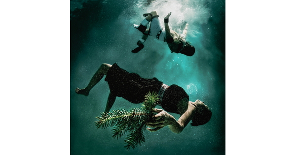 A color photograph of two people in Indigenous cultural dress floating under water.