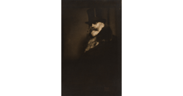 A dark sepia-toned portrait photograph of a White man with a white beard and dark mustache, wearing a top hat, glasses, and a fur coat.