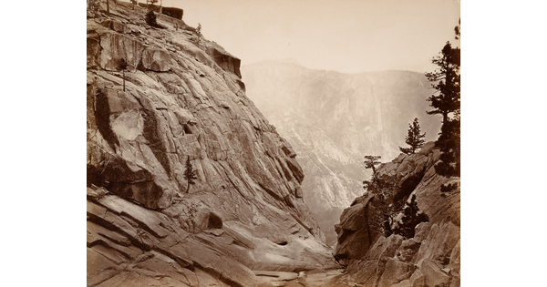 A sepia-toned photograph of a dry creek bed between two steep rocky hills.